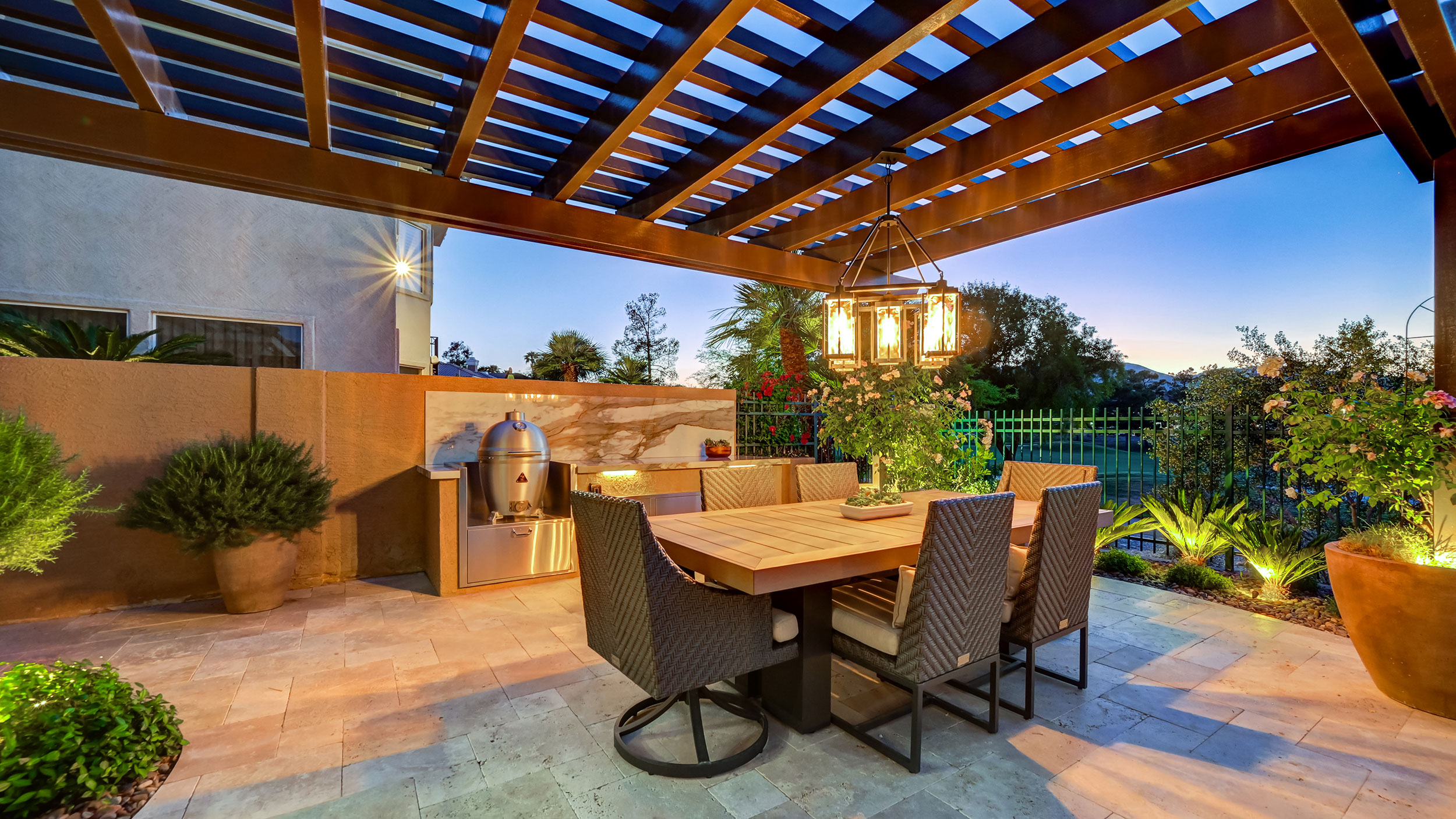 Stylish outdoor dining area under a wooden pergola, featuring a large table and lantern.